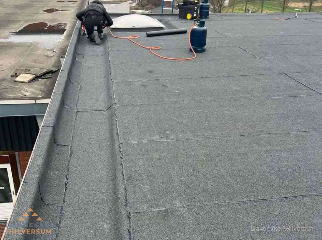 Dakdekker repareert bitumen dakbedekking op groot plat dak in Hilversum
